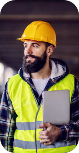 Portrait of highly motivated caucasian hardworking smiling bearded supervisor with helmet on head in vest and with laptop in hands posing on construct